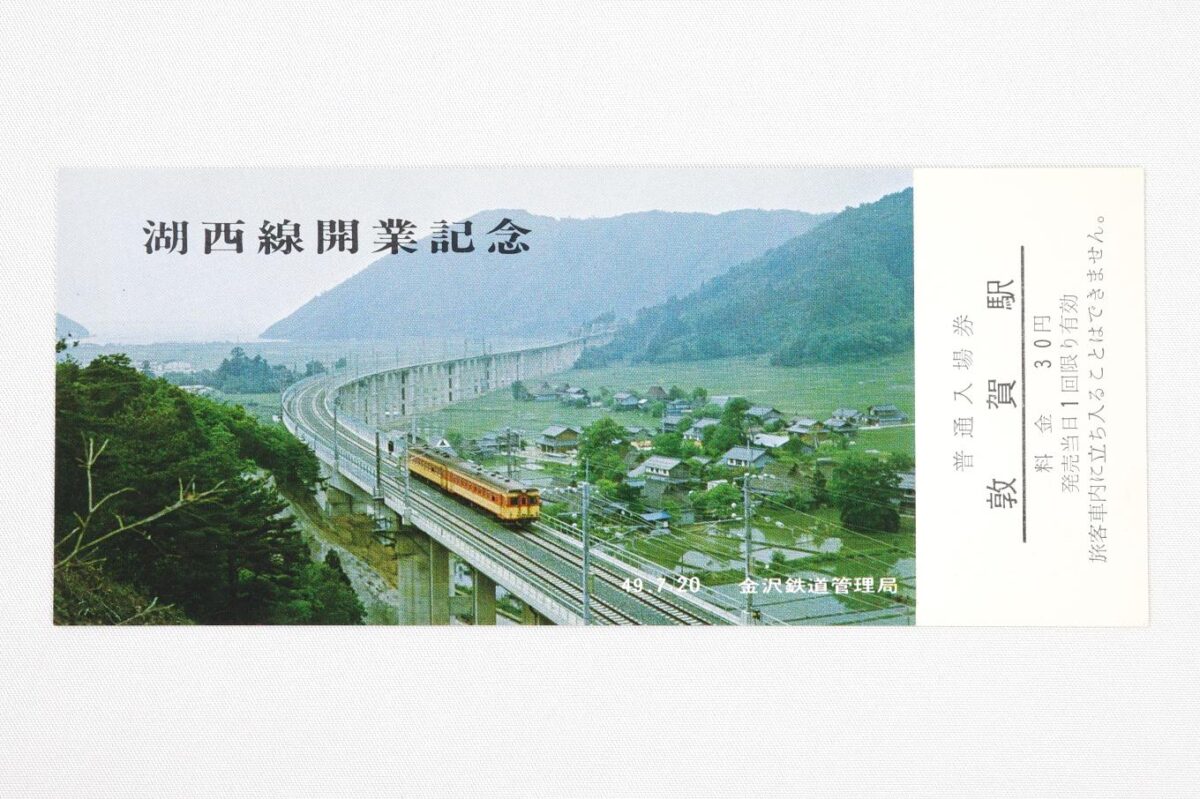 入場券の表面。遠くに琵琶湖を望む複線電化の高架線をゆく、2両編成のディーゼルカーの写真に、湖西線開業記念の文字が記されている。サイズは15.2 × 6.4 cm。